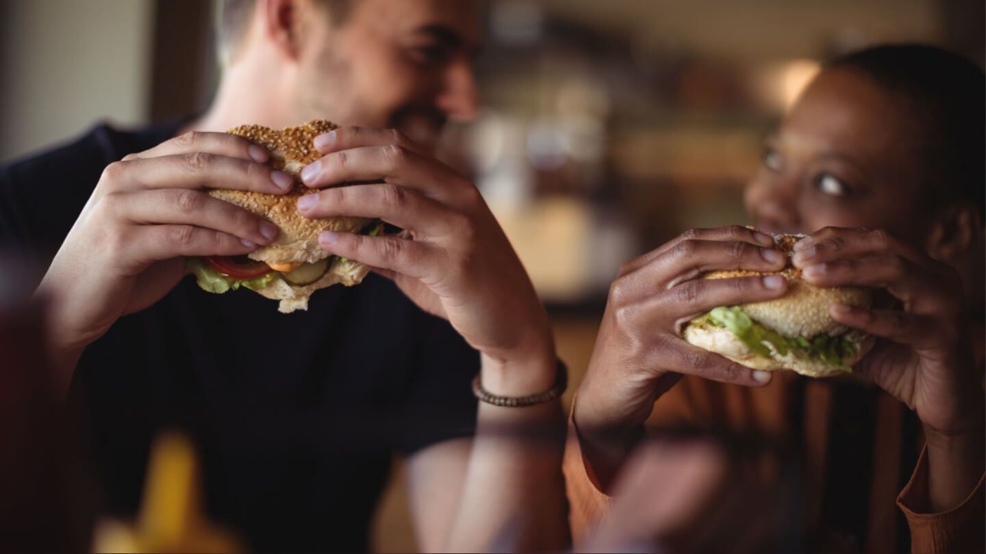 Two people enjoying hamburgers, with the hamburgers in focus and the people out of focus.